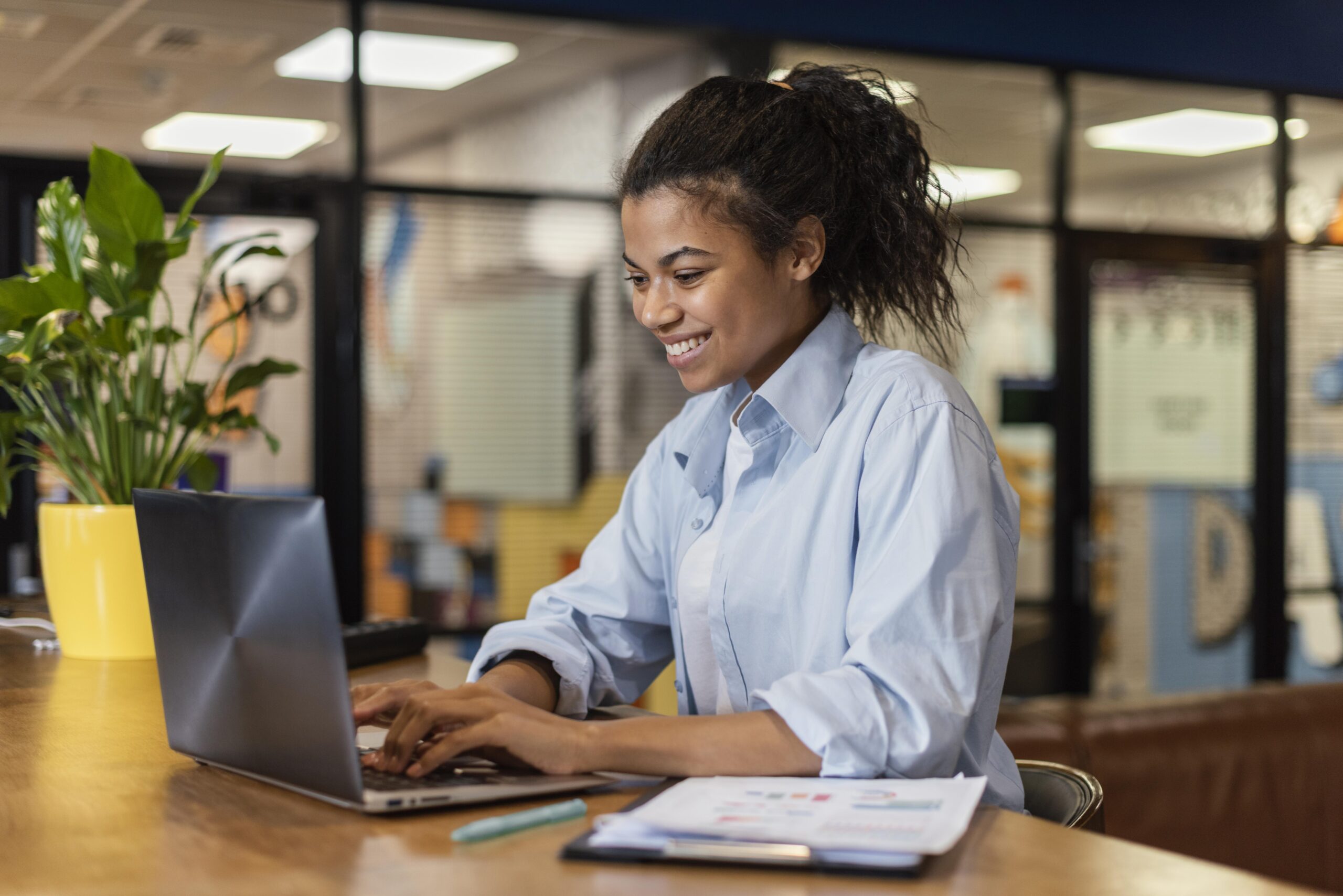 vista-lateral-de-uma-mulher-sorridente-trabalhando-com-um-laptop-no-escritorio